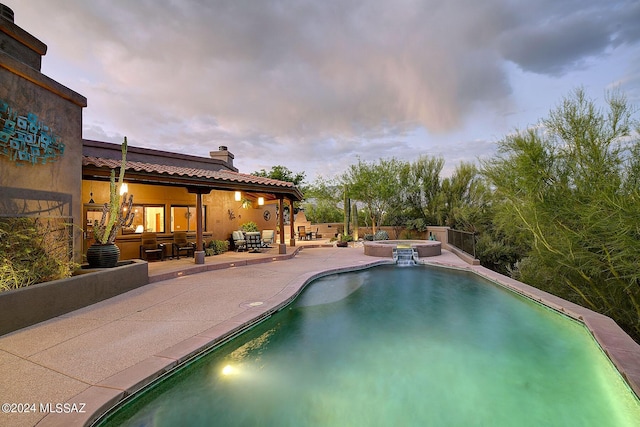 pool at dusk with an in ground hot tub and a patio area