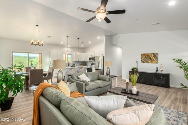 living area with visible vents, baseboards, light wood-style floors, ceiling fan with notable chandelier, and vaulted ceiling