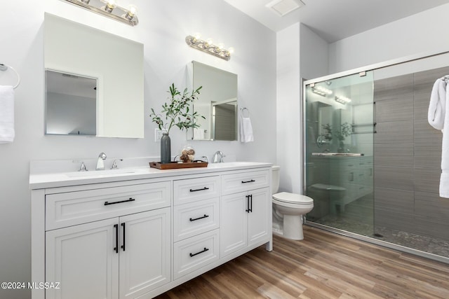 bathroom with toilet, a stall shower, a sink, wood finished floors, and double vanity