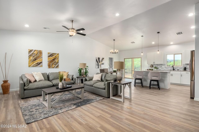 living room featuring light wood-type flooring, ceiling fan with notable chandelier, lofted ceiling, and visible vents