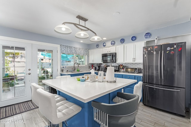 kitchen with a healthy amount of sunlight, stainless steel refrigerator, pendant lighting, and white cabinets