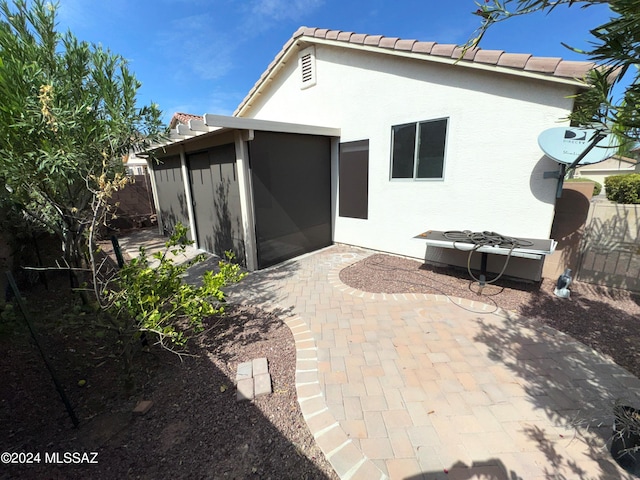 rear view of house with fence, a patio, stucco siding, a sunroom, and a tile roof