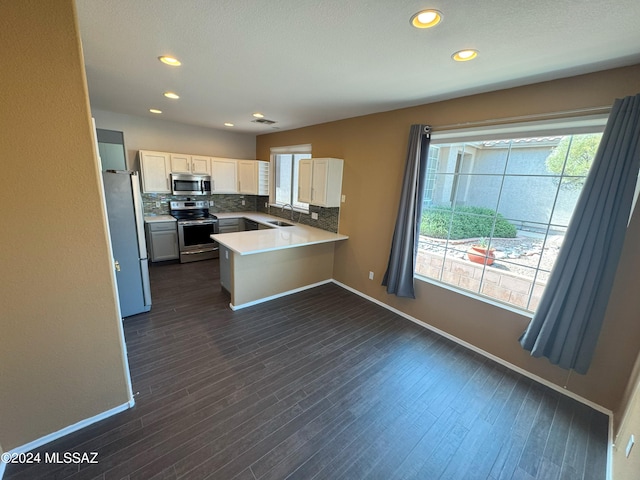 kitchen featuring dark hardwood / wood-style floors, stainless steel appliances, kitchen peninsula, backsplash, and white cabinetry