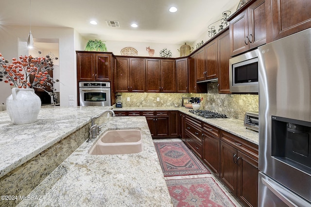 kitchen with light stone counters, tasteful backsplash, appliances with stainless steel finishes, and hanging light fixtures