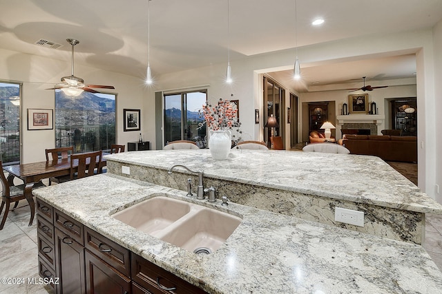 kitchen featuring light stone counters, ceiling fan, vaulted ceiling, sink, and decorative light fixtures