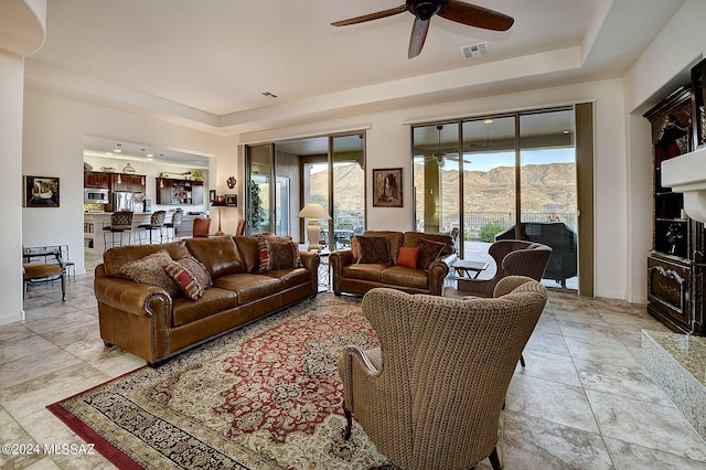 tiled living room with a mountain view, ceiling fan, a tray ceiling, and a wealth of natural light