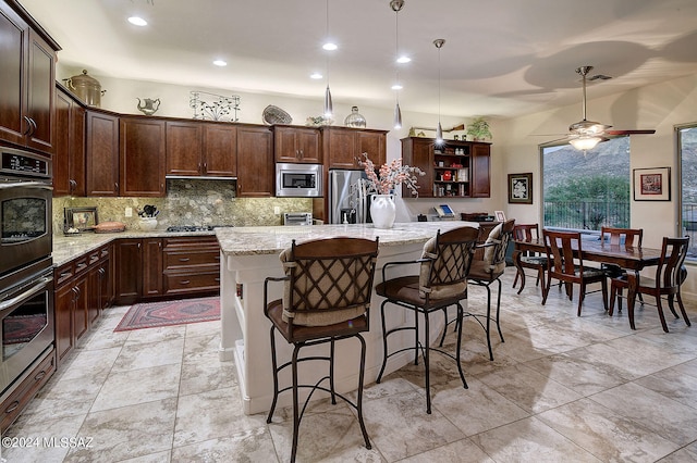 kitchen with light stone counters, ceiling fan, stainless steel appliances, pendant lighting, and a center island