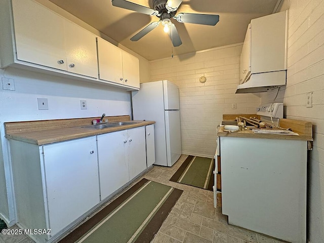 kitchen featuring white cabinets, brick patterned floor, a sink, freestanding refrigerator, and ceiling fan