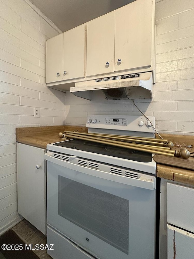 kitchen with white cabinets, concrete block wall, under cabinet range hood, and electric stove