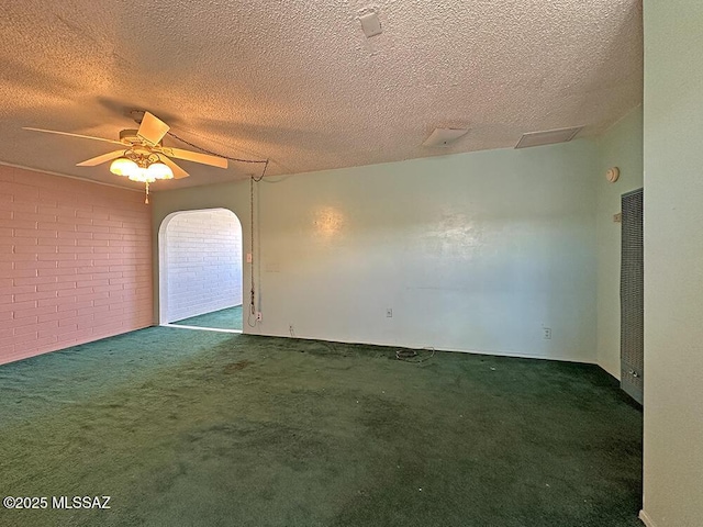 carpeted empty room featuring arched walkways, a textured ceiling, brick wall, and ceiling fan