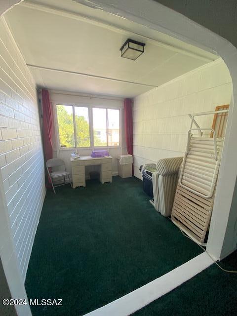 interior space featuring brick wall and dark colored carpet