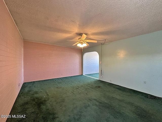 carpeted empty room featuring brick wall, a ceiling fan, and a textured ceiling