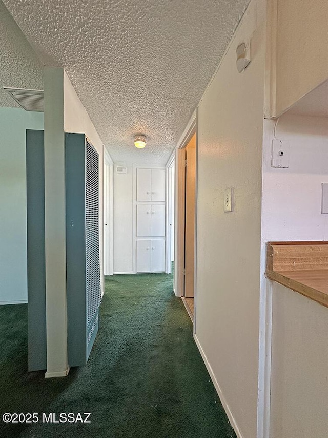 corridor with carpet floors, a textured ceiling, baseboards, and a heating unit