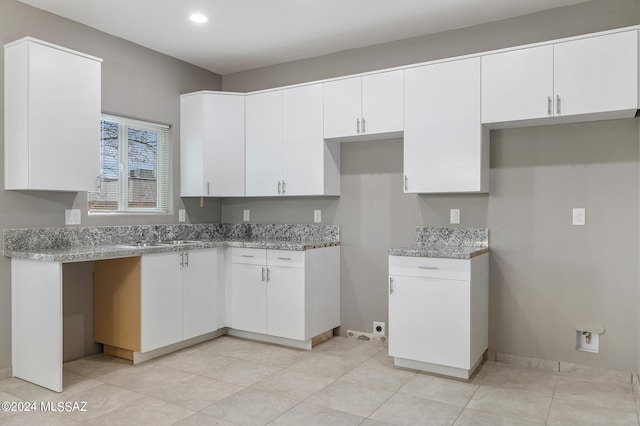 kitchen with light tile patterned flooring, sink, light stone counters, and white cabinetry