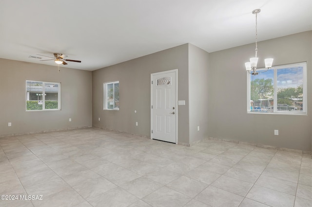 tiled spare room featuring ceiling fan with notable chandelier