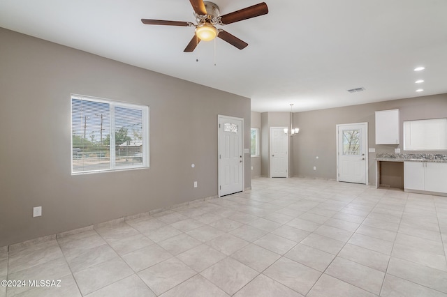 unfurnished living room with ceiling fan with notable chandelier, light tile patterned floors, and a wealth of natural light