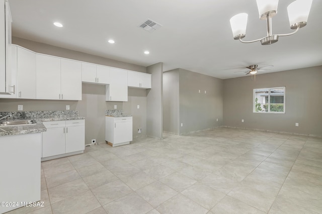 kitchen with ceiling fan with notable chandelier, sink, light stone counters, hanging light fixtures, and white cabinetry