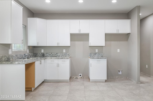 kitchen featuring light stone counters, white cabinets, light tile patterned floors, and sink