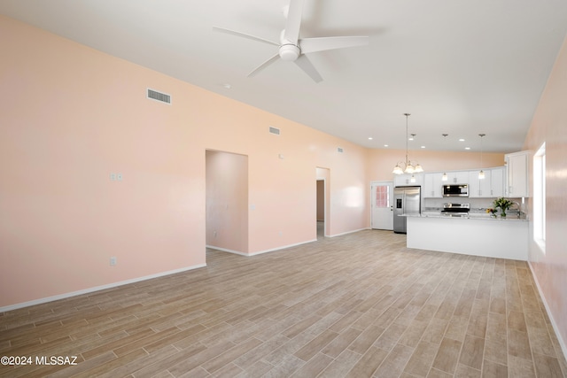 unfurnished living room with light hardwood / wood-style floors, vaulted ceiling, and ceiling fan with notable chandelier