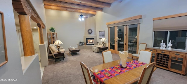 carpeted dining space with a large fireplace, ceiling fan, beam ceiling, and a high ceiling