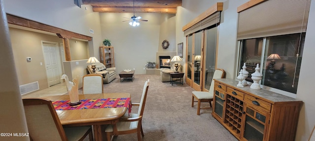 dining room with ceiling fan, beam ceiling, light colored carpet, and a towering ceiling