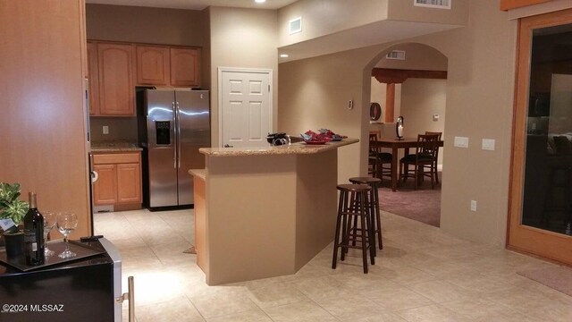 kitchen with light stone countertops, kitchen peninsula, stainless steel fridge, a breakfast bar, and light tile patterned flooring