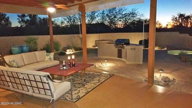 patio terrace at dusk featuring outdoor lounge area, ceiling fan, a grill, and exterior kitchen