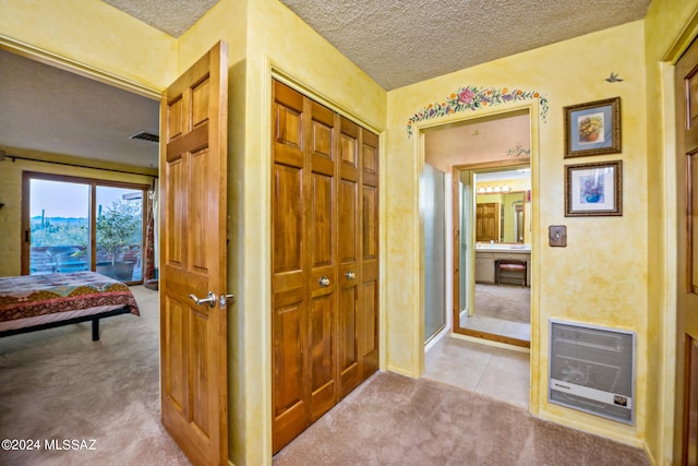 corridor with light carpet, heating unit, and a textured ceiling