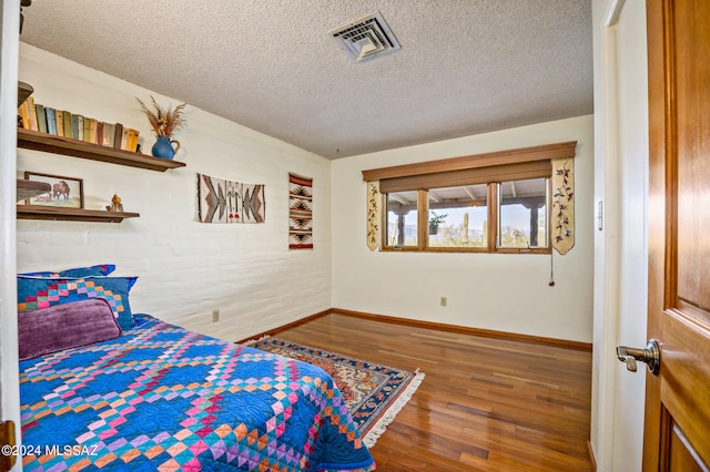 bedroom featuring brick wall, wood-type flooring, and a textured ceiling