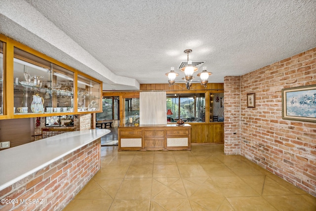 kitchen with pendant lighting, light tile patterned floors, brick wall, a textured ceiling, and an inviting chandelier