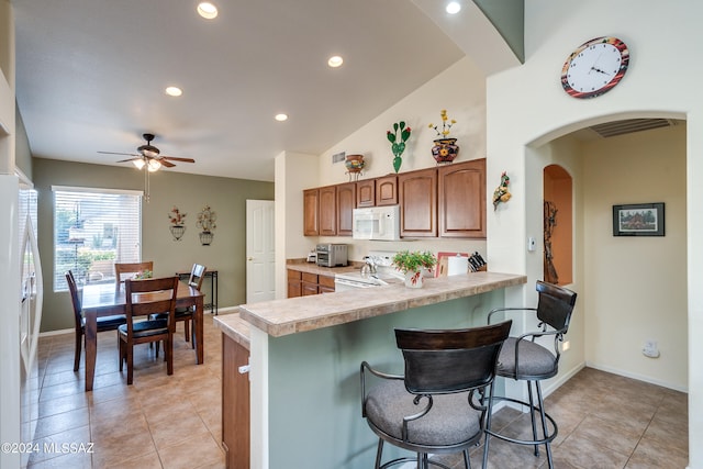 kitchen with white appliances, a breakfast bar, kitchen peninsula, and ceiling fan