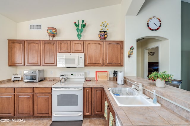 kitchen with white appliances, sink, tile counters, lofted ceiling, and light tile patterned floors