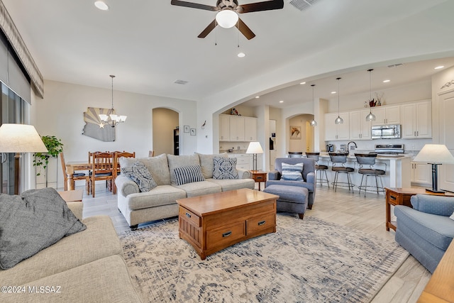 living room with ceiling fan with notable chandelier, light hardwood / wood-style flooring, and sink