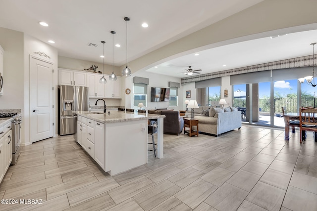 kitchen with stainless steel appliances, white cabinetry, decorative light fixtures, sink, and an island with sink