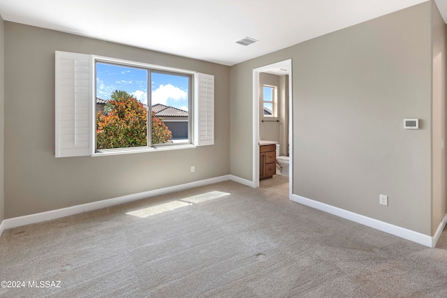 unfurnished bedroom featuring light colored carpet and ensuite bath