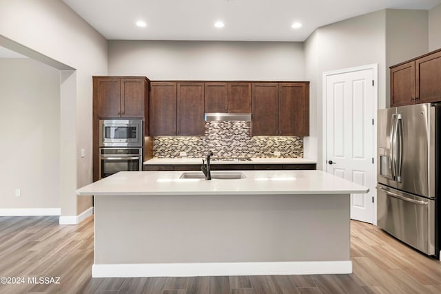 kitchen with a center island with sink, appliances with stainless steel finishes, sink, and light wood-type flooring