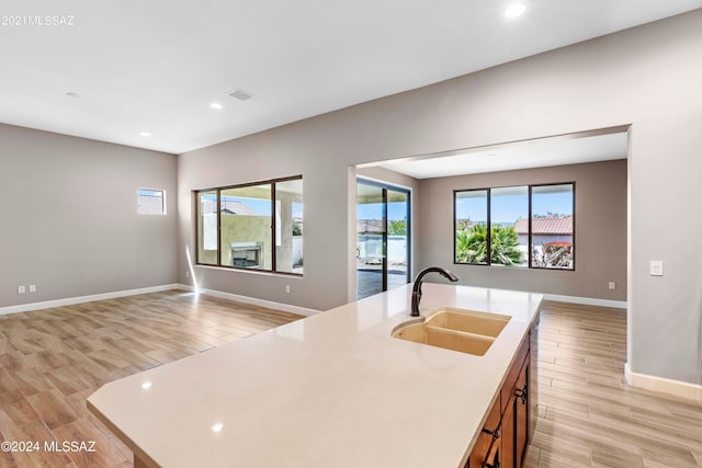 kitchen with an island with sink, sink, and light wood-type flooring