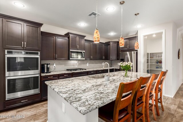 kitchen with appliances with stainless steel finishes, pendant lighting, tasteful backsplash, and an island with sink