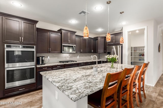 kitchen featuring a breakfast bar, decorative light fixtures, sink, a kitchen island with sink, and stainless steel appliances