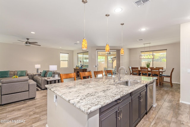 kitchen with light stone countertops, sink, pendant lighting, and a center island with sink