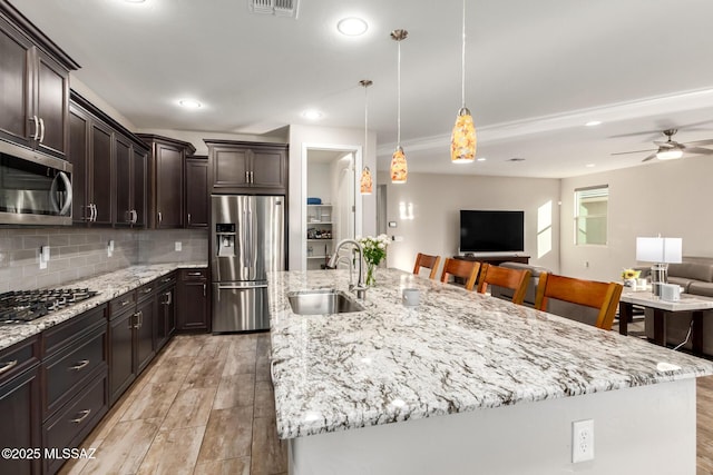 kitchen featuring appliances with stainless steel finishes, decorative light fixtures, sink, a kitchen breakfast bar, and a large island with sink