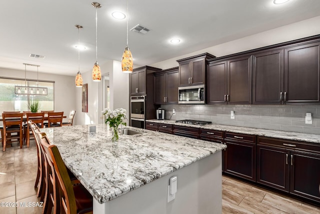 kitchen with hanging light fixtures, a center island with sink, a breakfast bar area, and appliances with stainless steel finishes