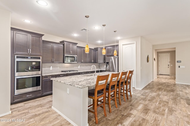 kitchen with stainless steel appliances, a center island with sink, a kitchen bar, decorative light fixtures, and light hardwood / wood-style floors