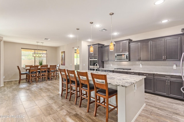 kitchen with decorative backsplash, a kitchen island with sink, a breakfast bar area, stainless steel appliances, and pendant lighting