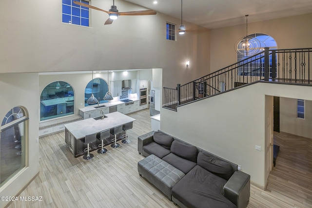 living room with light hardwood / wood-style flooring, a towering ceiling, and ceiling fan with notable chandelier