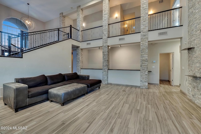 living room with a high ceiling, light hardwood / wood-style floors, ornate columns, and a notable chandelier