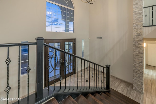 stairway with wood-type flooring, french doors, and a high ceiling