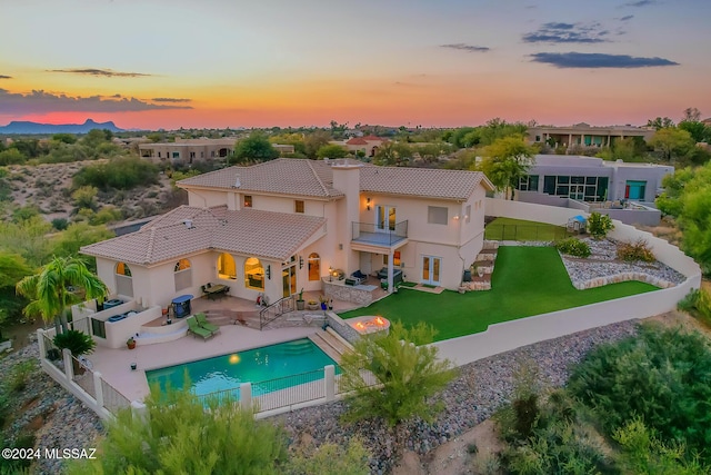 back house at dusk featuring outdoor lounge area, a yard, a balcony, and a patio area