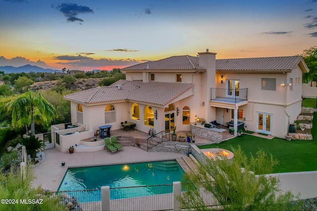 back house at dusk with a fenced in pool, a patio area, a balcony, and an outdoor kitchen