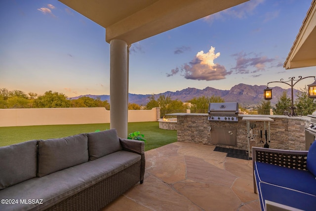 patio terrace at dusk with an outdoor kitchen, area for grilling, outdoor lounge area, a mountain view, and a yard